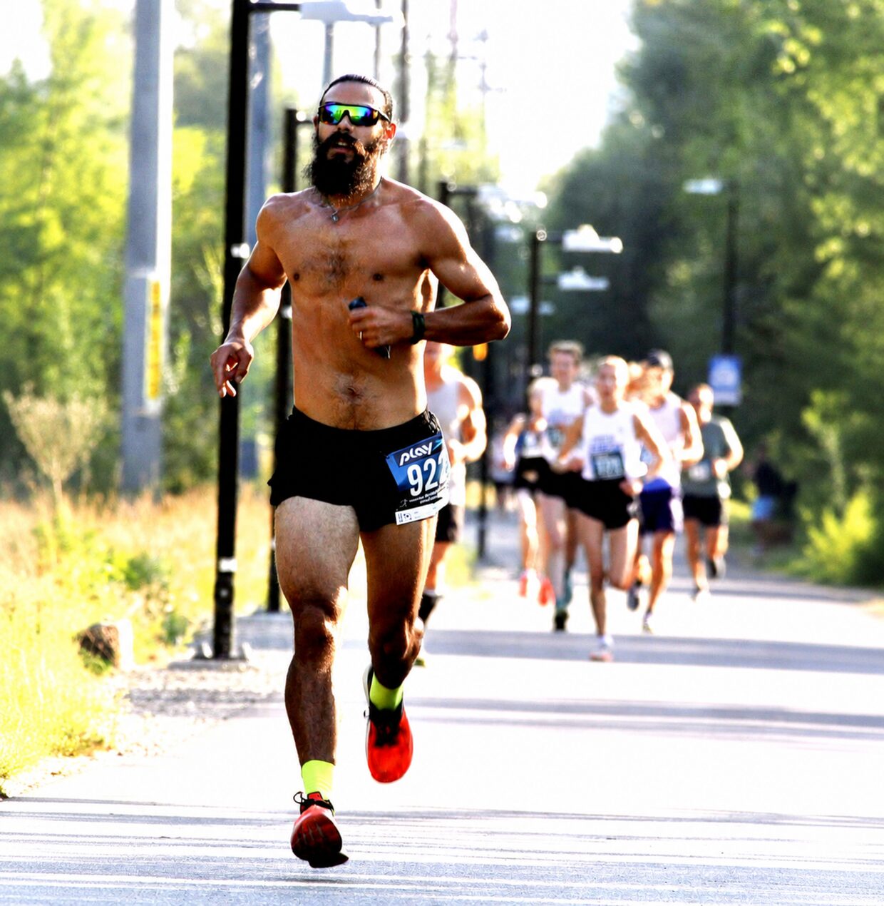 A lead runner racing shirtless on a sunny road in the summer heat